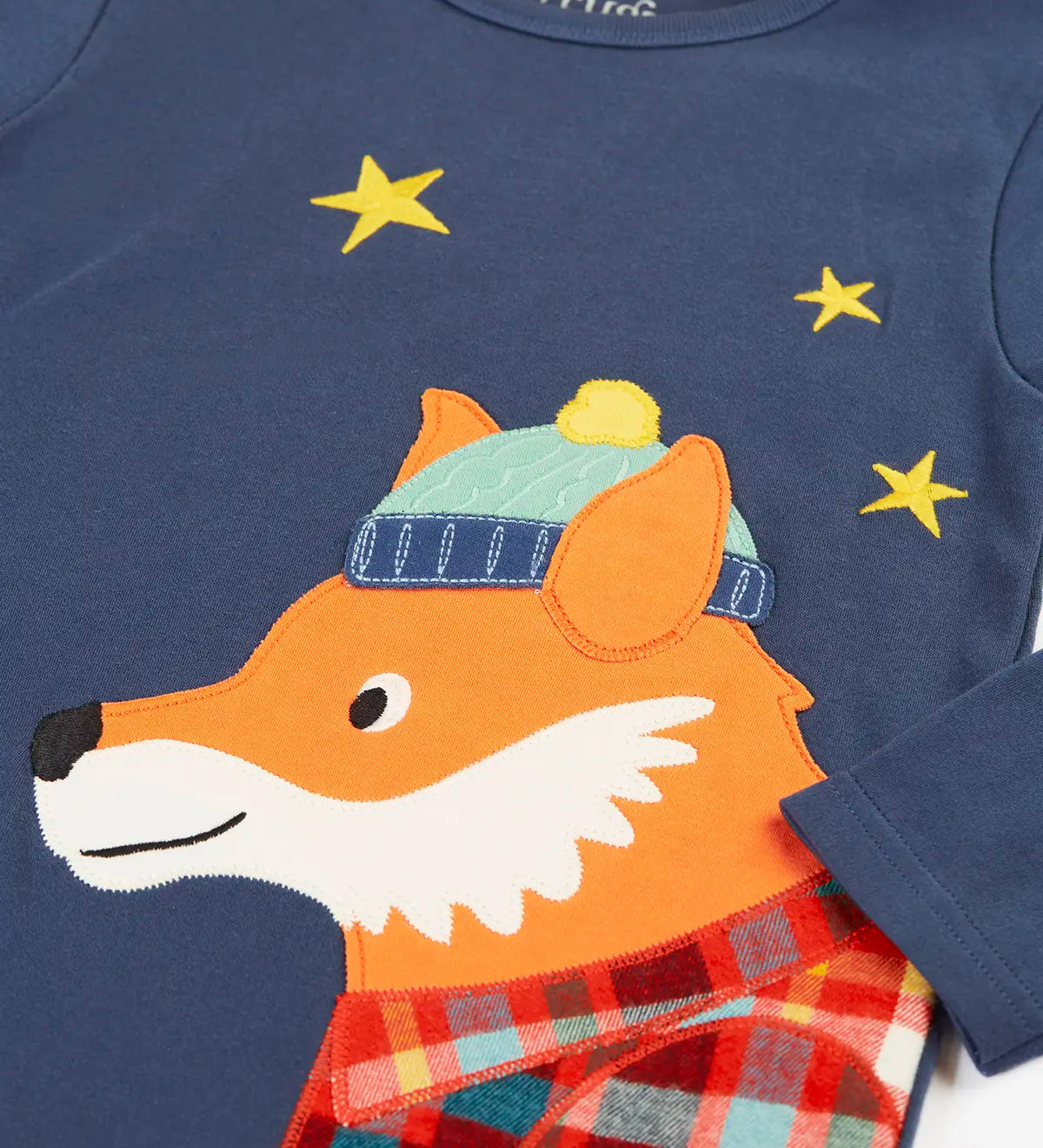 Close up of the fox applique on the long sleeved top from the Frugi organic cotton caden check festive fox pyjamas. The fox is wearing a blue bobble hat and a check shirt.