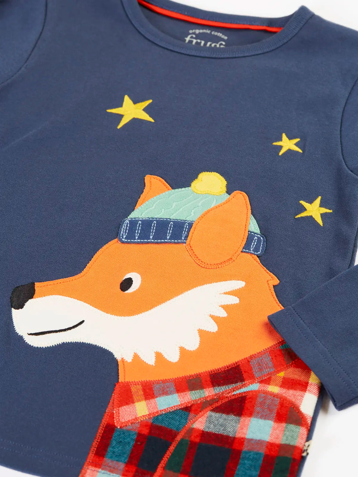 Close up of the fox applique on the long sleeved top from the Frugi organic cotton caden check festive fox pyjamas. The fox is wearing a blue bobble hat and a check shirt.