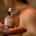 A person holding the Green People Age Defy+ Liquid Gold Tanning Drops 30ml bottle next to their skin