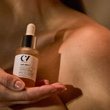 A person holding the Green People Age Defy+ Liquid Gold Tanning Drops 30ml bottle next to their skin