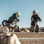 Two children playing near some rocks on their Early Rider Big Foot Balance Bikes, with a light blue sky in the background