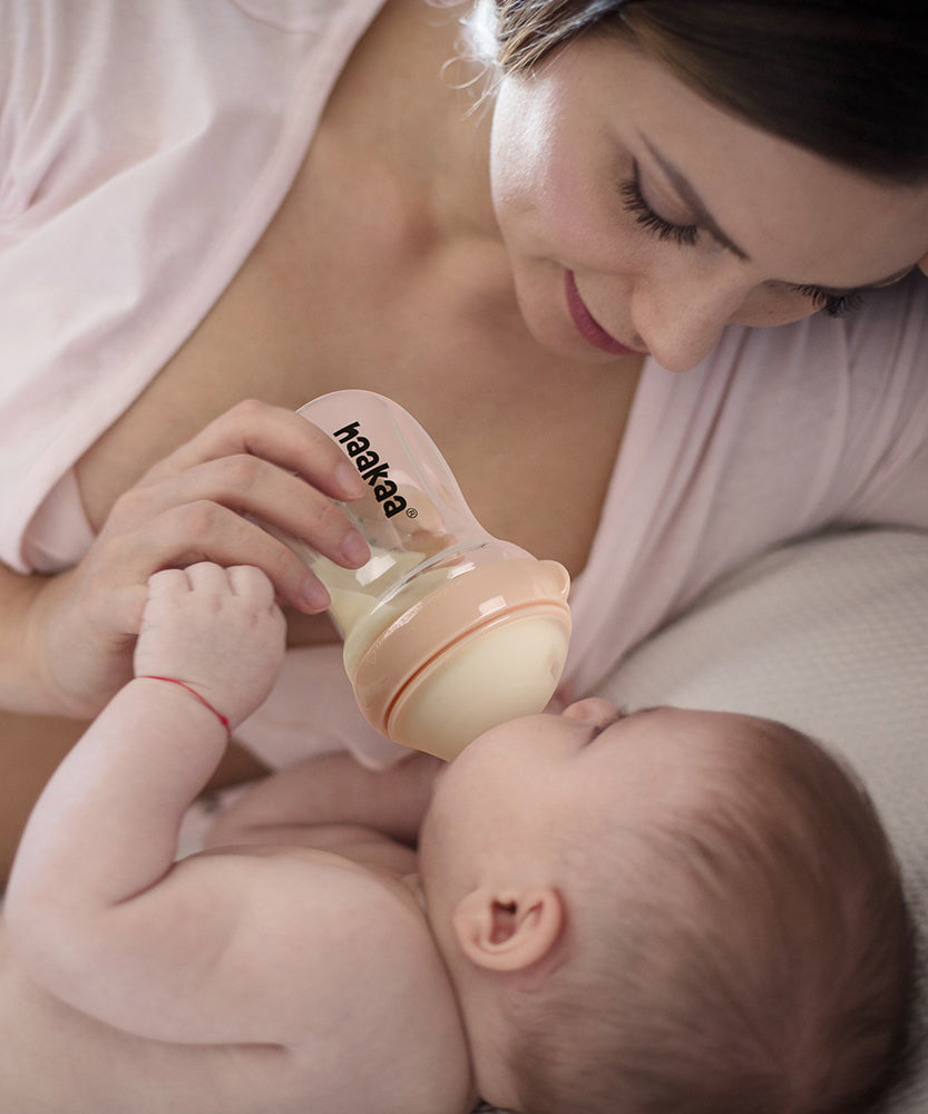 A parent feeding their child with the Haakaa Generation 3 Glass Baby Bottle in peach