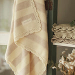 Avery Row Stripe Knit Organic Baby Blanket - Oat Melange, hanging on a dresser door with folded knitted blankets on the shelf. 