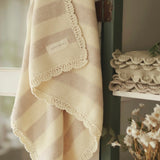 Avery Row Stripe Knit Organic Baby Blanket - Oat Melange, hanging on a dresser door with folded knitted blankets on the shelf. 