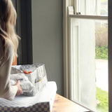 A person by a window, placing the Coastline Nappy Caddy on top of the Waves Changing Mat
