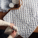 Avery Row Travel Changing Mat - Coastline in adults hands, unfolded on a wooden table, showing the pocket at the end of the mat.