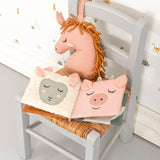 The Roommate Baby Nursery Book - Country Life laid open on a small wooden chair, showing the sheep and pig fabric pages. There is a pink Roommate toy behind the book