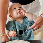 A child eating food at a table whilst wearing the Roommate Organic Cotton Baby Bib - Koala