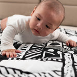 A baby looking at the monochromatic, black and white shapes on the Etta Loves x Camille Walala Reversible Playmat