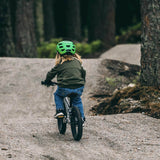 Child riding a bicycle on a path in a forest, facing away from the camera
