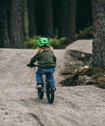 Child riding a bicycle on a path in a forest, facing away from the camera