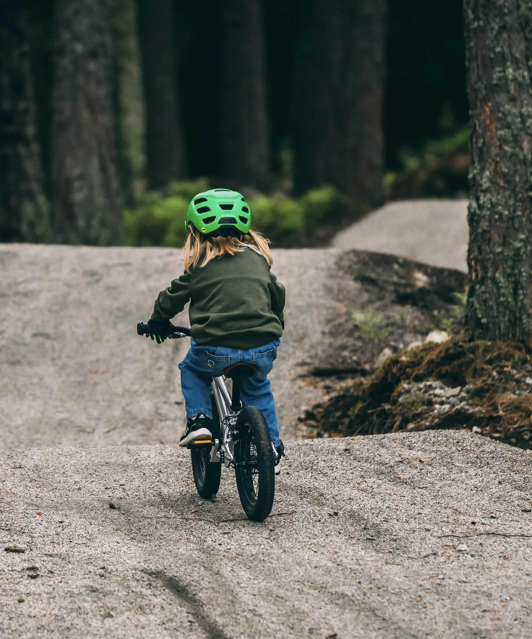 Child riding a bicycle on a path in a forest, facing away from the camera
