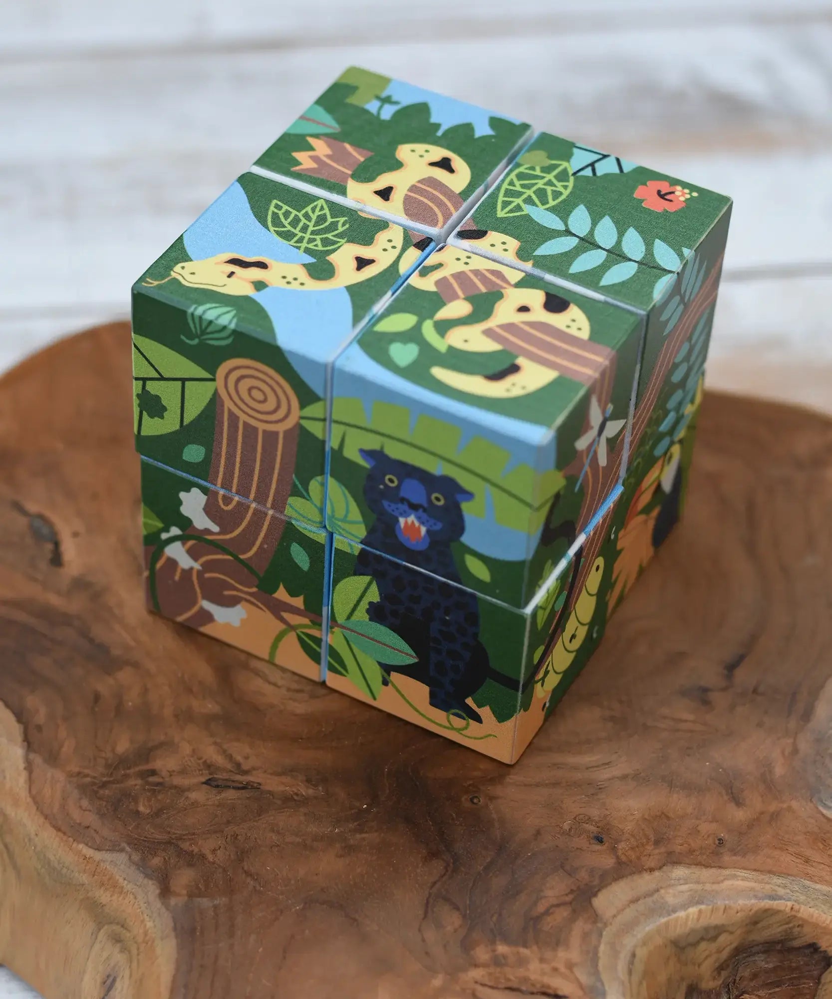Bajo 2-in-1 polar jungle wooden cube block puzzle placed on a wooden surface shown on the jungle side with a jaguar on one side and a snake on the other.