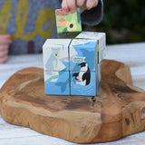 A child's hand is placing a colorful animal block onto a stack of wooden educational blocks featuring polar animals like a penguin and polar bear, set on a rustic wooden serving board.