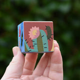 Hand holding a small square wooden block from The Bajo 2-in-1 desert reef cube puzzle block set. 