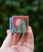 Hand holding a small square wooden block from The Bajo 2-in-1 desert reef cube puzzle block set. 