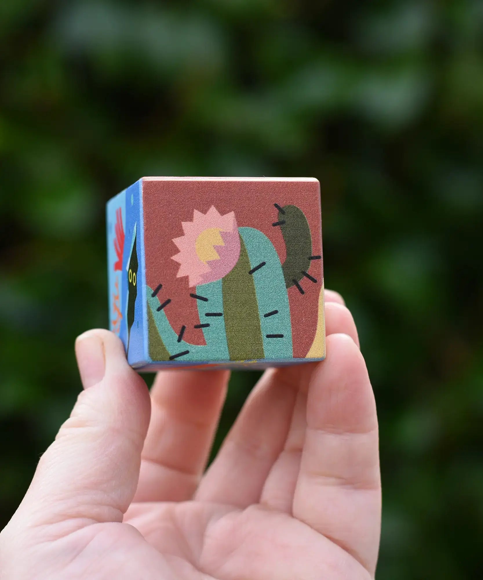 Hand holding a small square wooden block from The Bajo 2-in-1 desert reef cube puzzle block set. 