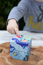 Child's hand pointing at the pink jelly fish on the Bajo 2-in-1 reef desert wooden cube block puzzle blocks. 