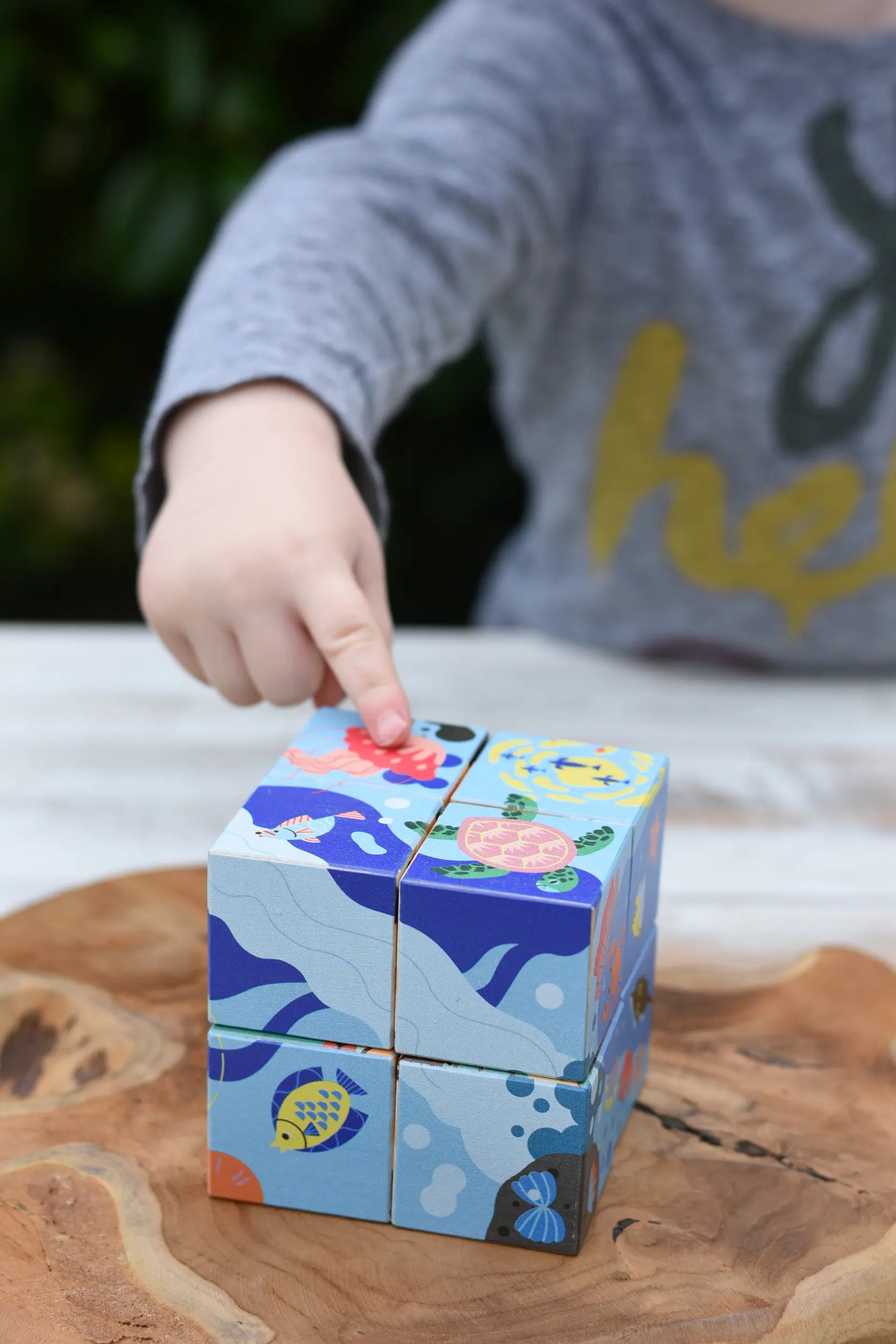 Child's hand pointing at the pink jelly fish on the Bajo 2-in-1 reef desert wooden cube block puzzle blocks. 