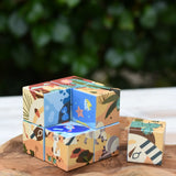 Bajo 2-in-1 reef desert wooden cube block puzzle placed on a wooden surface with one block taken out of the cube. The desert design illustration can be seen on the outside with the reef design showing on the other.