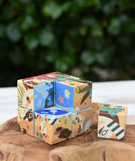 Bajo 2-in-1 reef desert wooden cube block puzzle placed on a wooden surface with one block taken out of the cube. The desert design illustration can be seen on the outside with the reef design showing on the other.