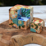 Bajo 2-in-1 reef desert wooden cube block puzzle, set of colorful, patterned wooden blocks with illustrated animal and nature designs, arranged on a rustic wooden board outdoors.
