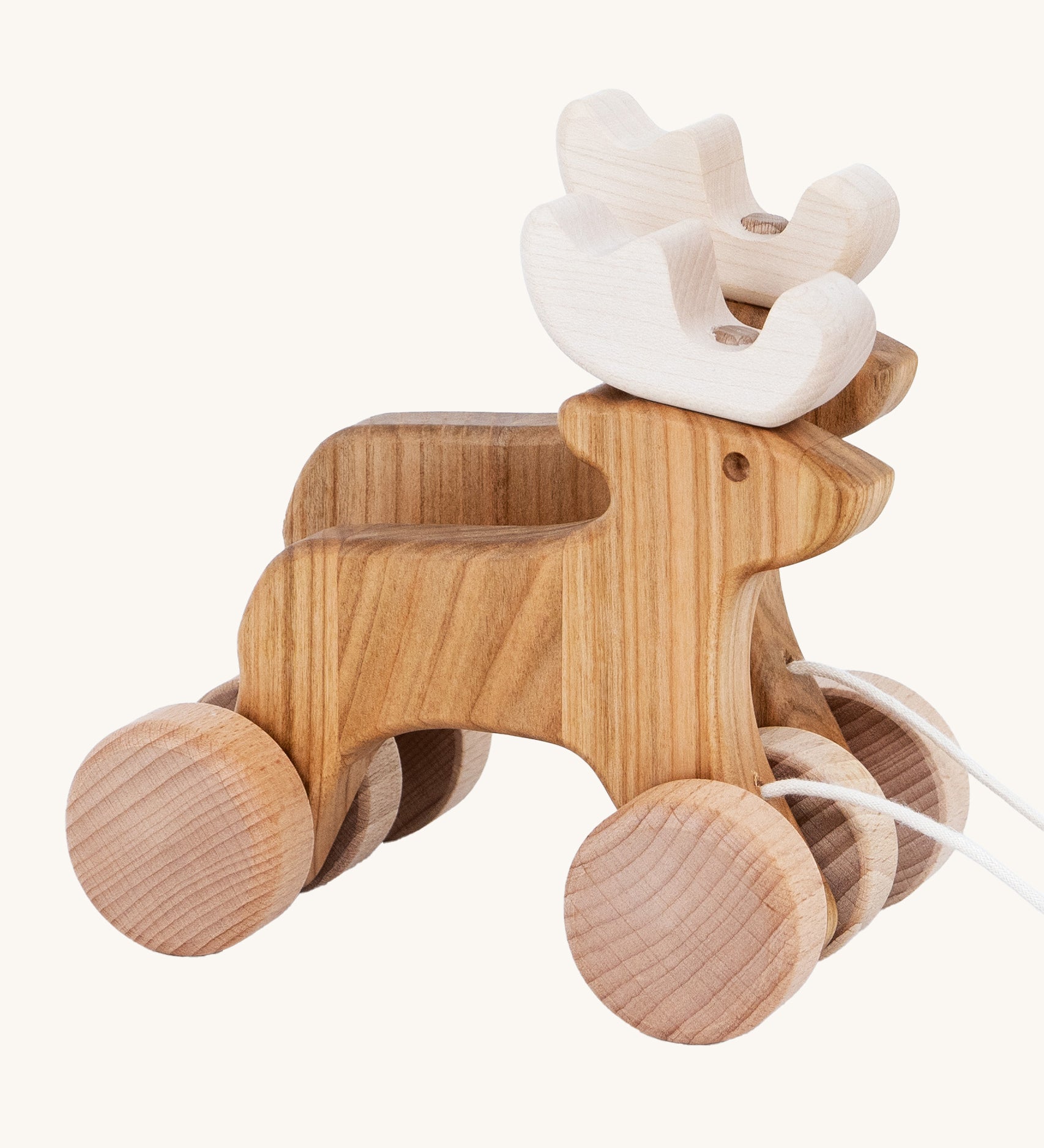 A side on view of the Bajo Pull Along Jumping Reindeer, showing the natural wood and white antlers of the reindeer. The image also shows how the two reindeer's are attached together by two wooden wheels. The image is on a cream background