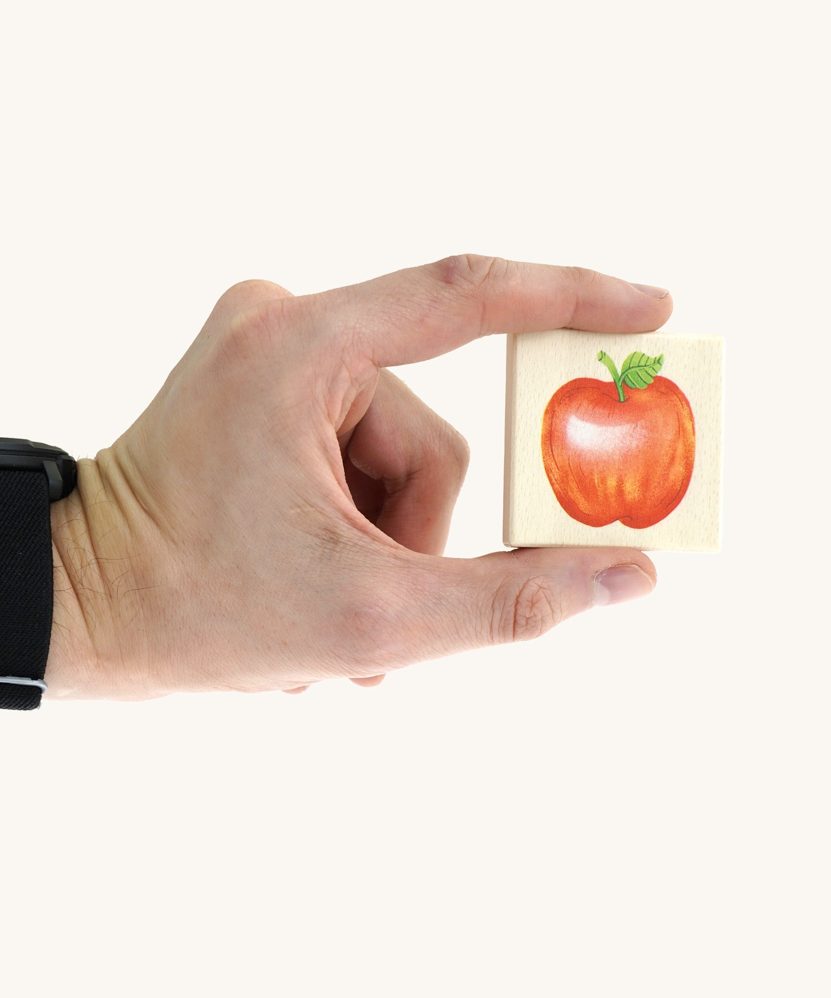 An adult hand holding a square tile from the Bajo classic memory game available at Babipur showing an apple illustration and the scale of the tile