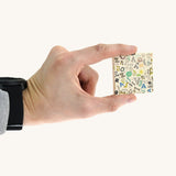 An adult hand holding a square tile from the Bajo classic memory game available at Babipur showing the underside detail and the scale of the tile