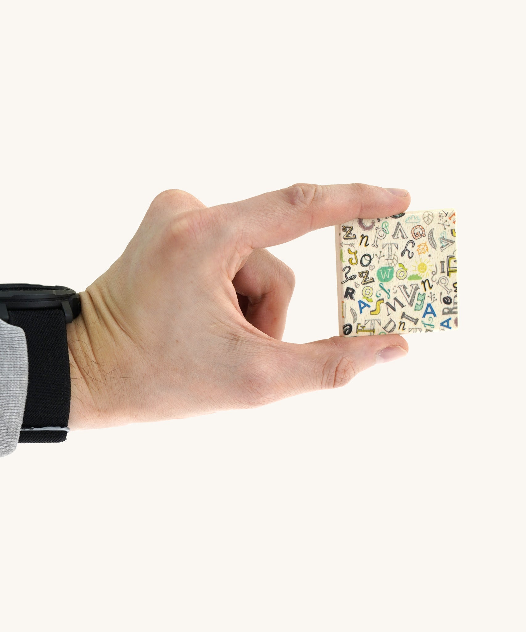 An adult hand holding a square tile from the Bajo classic memory game available at Babipur showing the underside detail and the scale of the tile