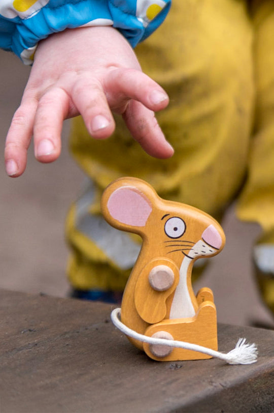 Child's hand reaching out for a wooden Bajo Gruffalo mouse toy to represent Bajo's Gruffalo toy range, for sale at Babipur, Bajo's official UK distroibutor.