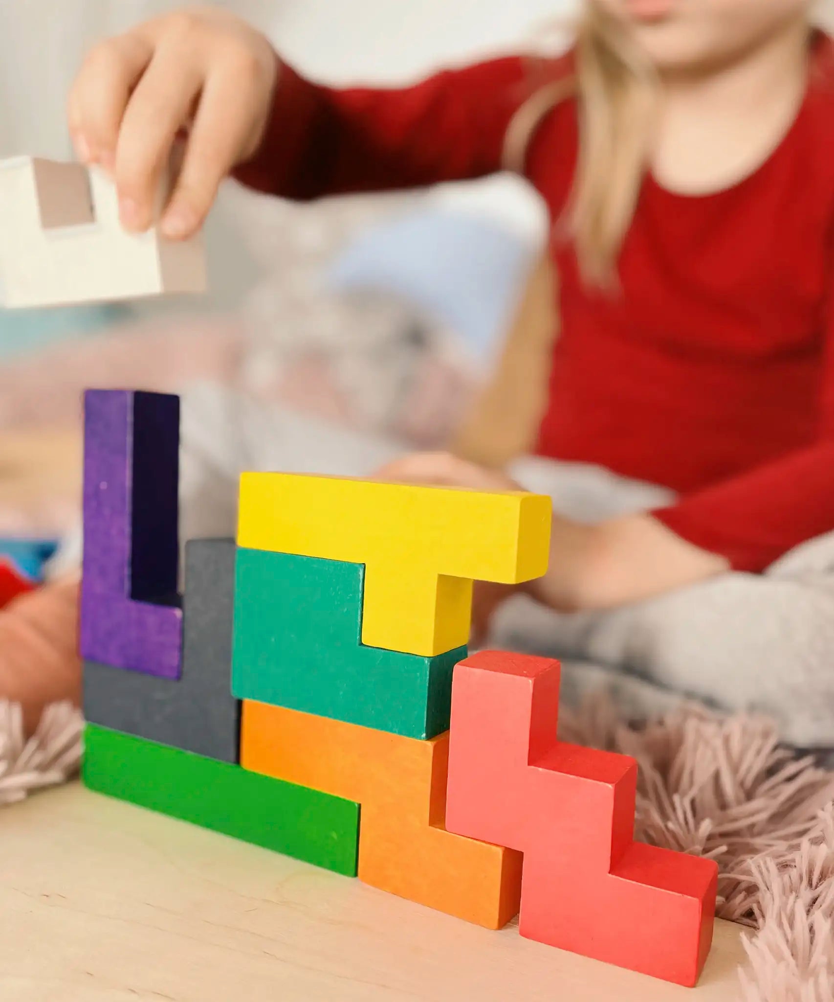 Child building a structure using different Bajo wooden coloured Pentomino puzzle blocks
