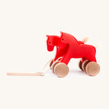 Bajo hand made wooden jumping horse in red and available at Babipur. Features unpainted wheels  and a toggle to pull along the horses