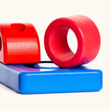 Wooden pieces from the Bajo puzzle tower stacker set showing a red ring, blue base and a red top piece