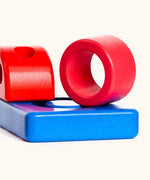 Wooden pieces from the Bajo puzzle tower stacker set showing a red ring, blue base and a red top piece