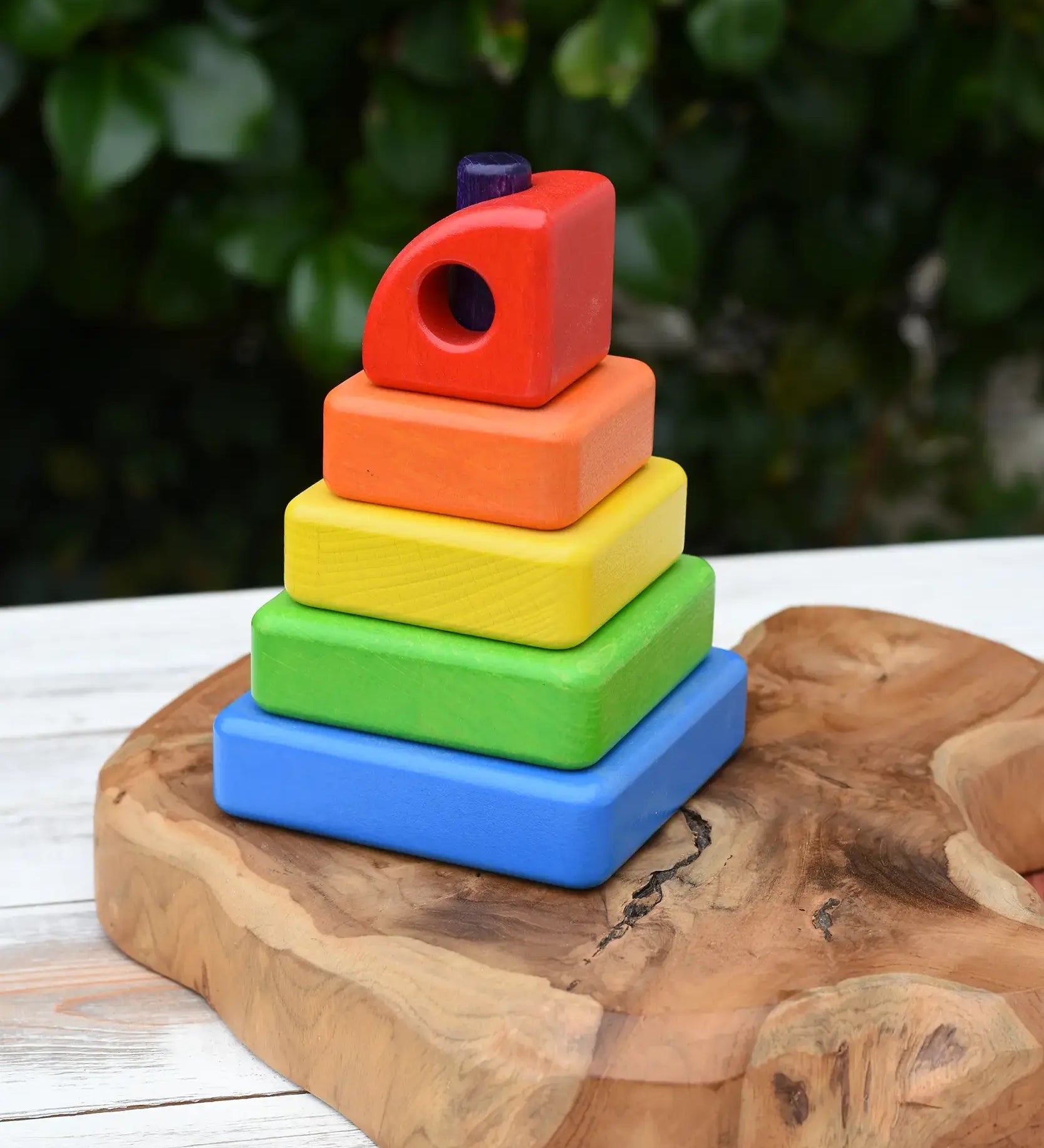 Bajo Puzzle Stacker Tower. A colorful wooden stacking toy set with five nested square blocks in blue, green, yellow, orange, and red, with a purple pole inside. 