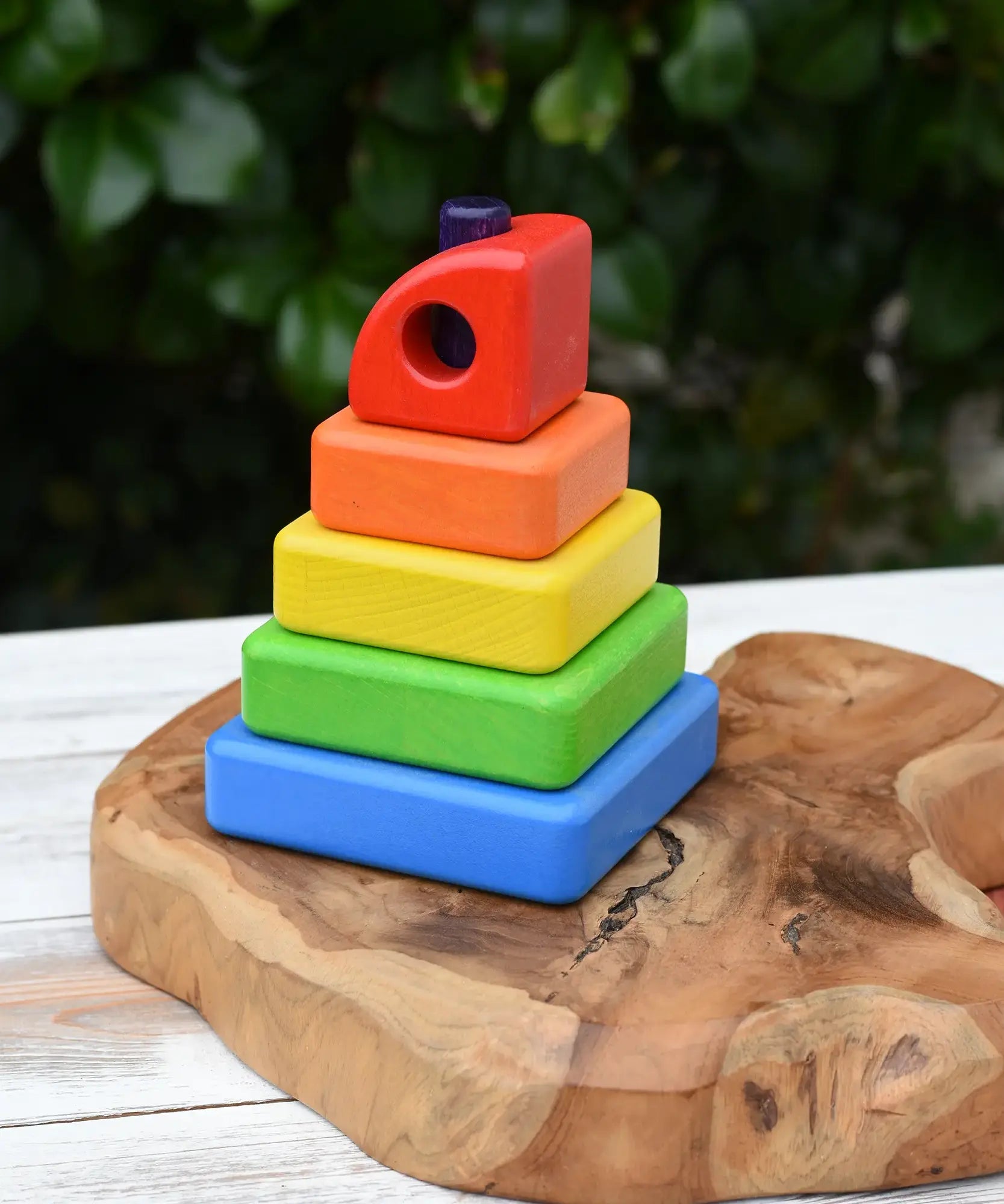 Bajo Puzzle Stacker Tower. A colorful wooden stacking toy set with five nested square blocks in blue, green, yellow, orange, and red, with a purple pole inside. 
