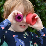 Child holding the cylider pieces from the Bajo Puzzle Stacker Tower up to his eyes. 