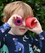 Child holding the cylider pieces from the Bajo Puzzle Stacker Tower up to his eyes. 