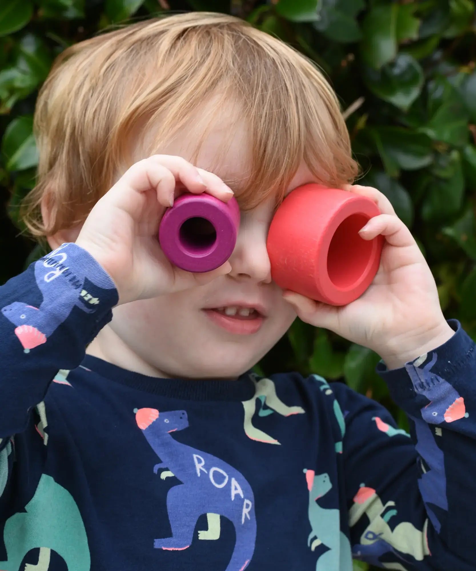 Child holding the cylider pieces from the Bajo Puzzle Stacker Tower up to his eyes. 