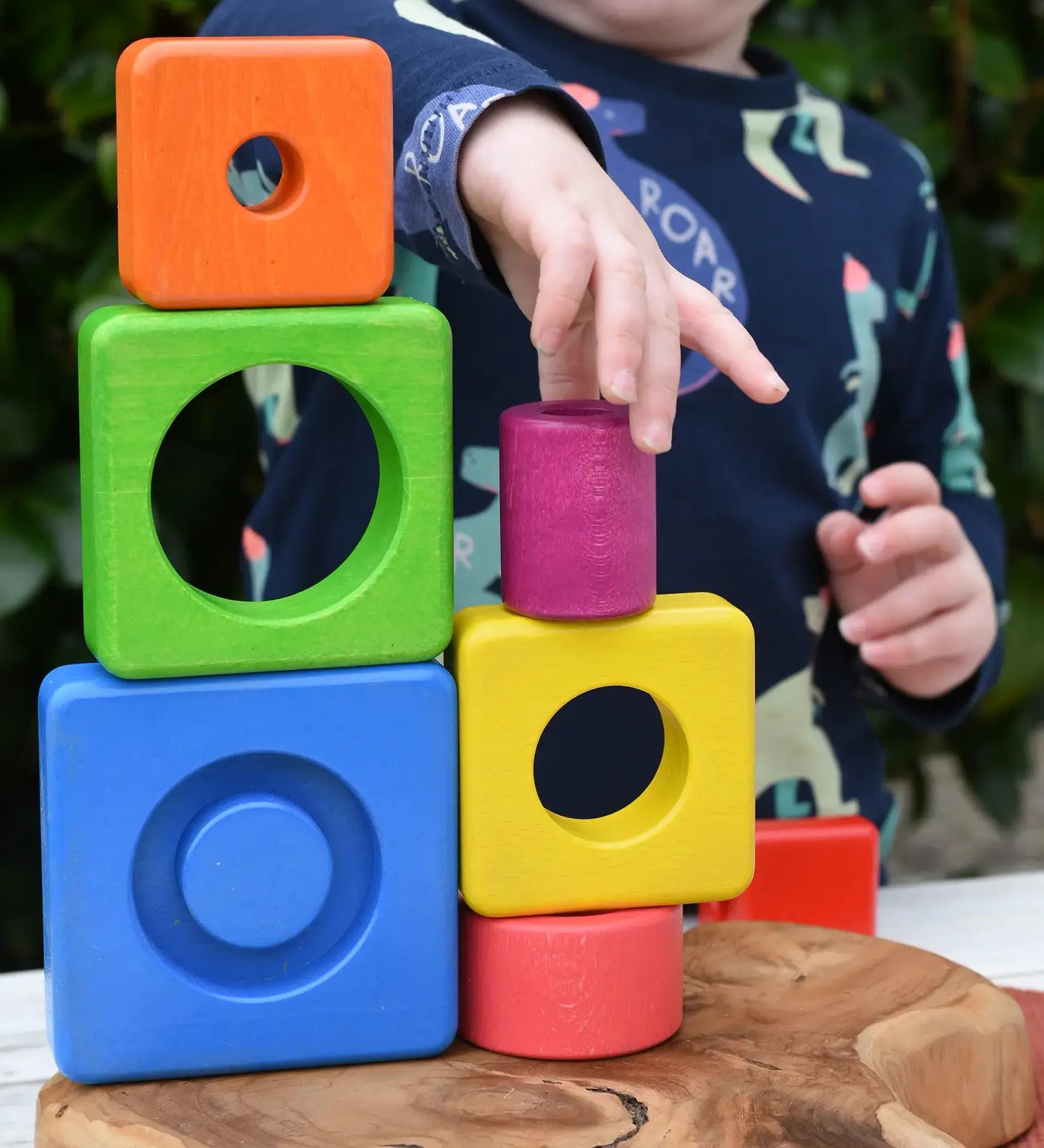 Child stacking colorful wooden blocks from the Bajo Puzzle Stacker Tower on top of each other.