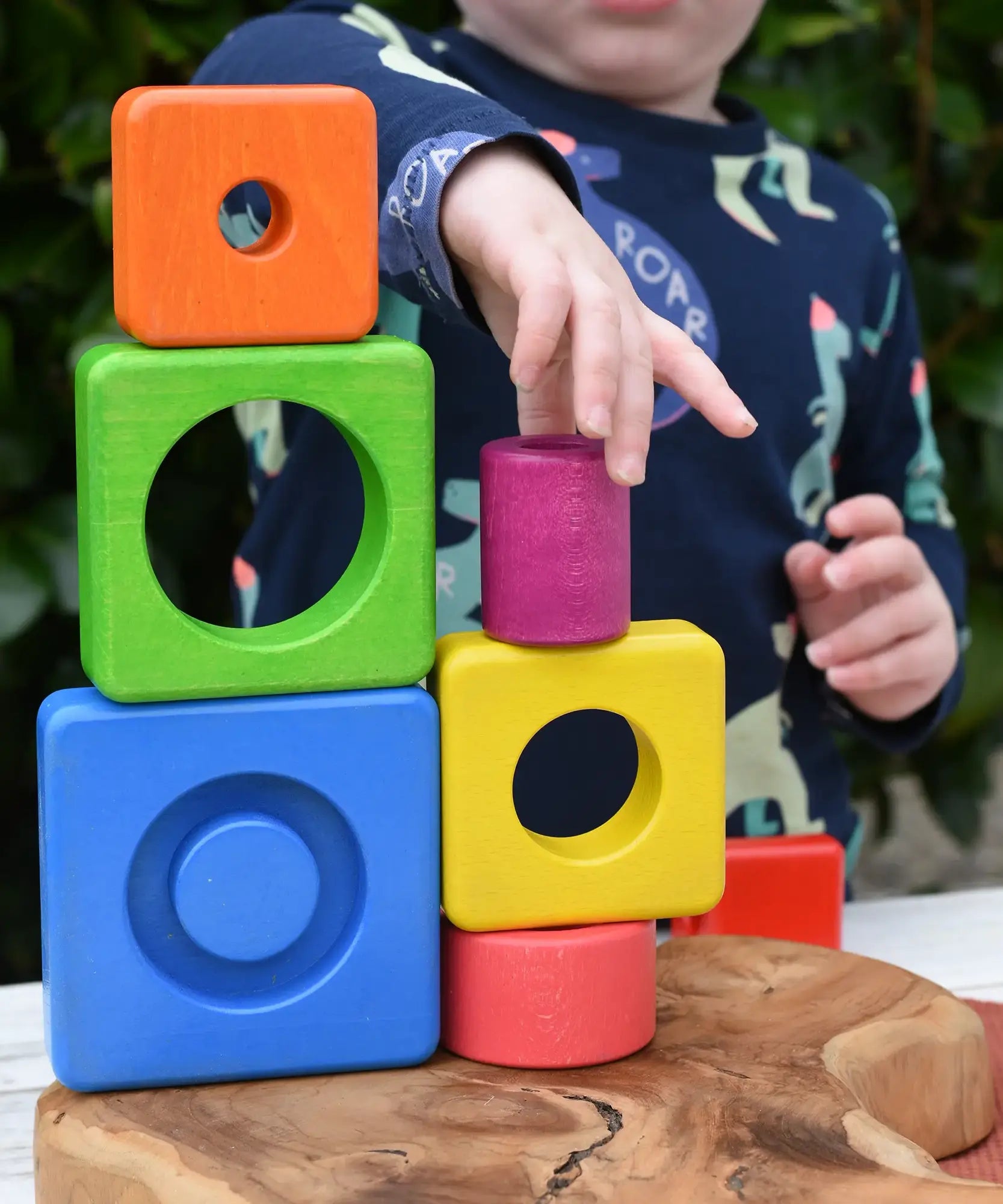 Child stacking colorful wooden blocks from the Bajo Puzzle Stacker Tower on top of each other.