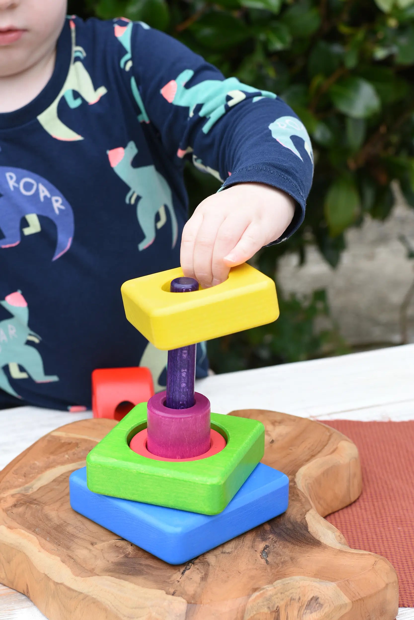 Child stacking the pieces from the Bajo Puzzle Stacker Tower onto the purple pole.