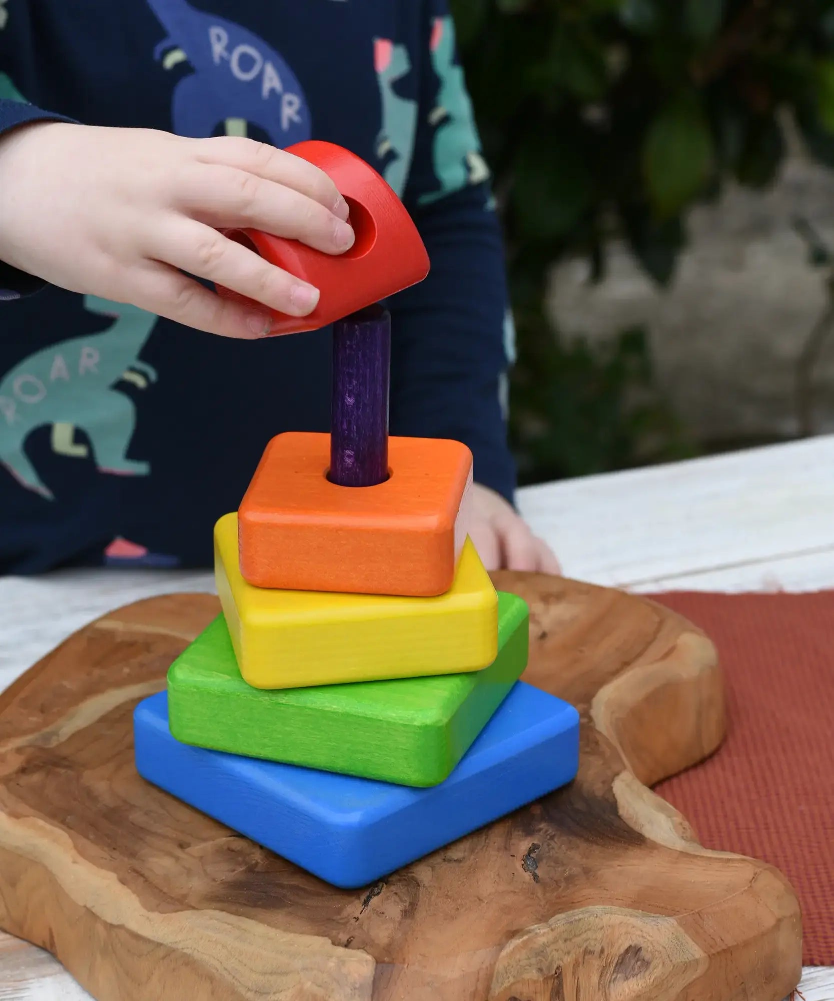 Child's hand placing the top red coloured block onto the top pf the Bajo Puzzle Stacker Tower.