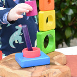 Child playing with the Bajo Puzzle Stacker Tower, lifting the pink cylinder piece that keeps the purple centre pole in place from the base.
