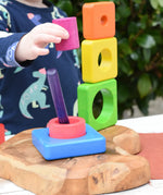Child playing with the Bajo Puzzle Stacker Tower, lifting the pink cylinder piece that keeps the purple centre pole in place from the base.