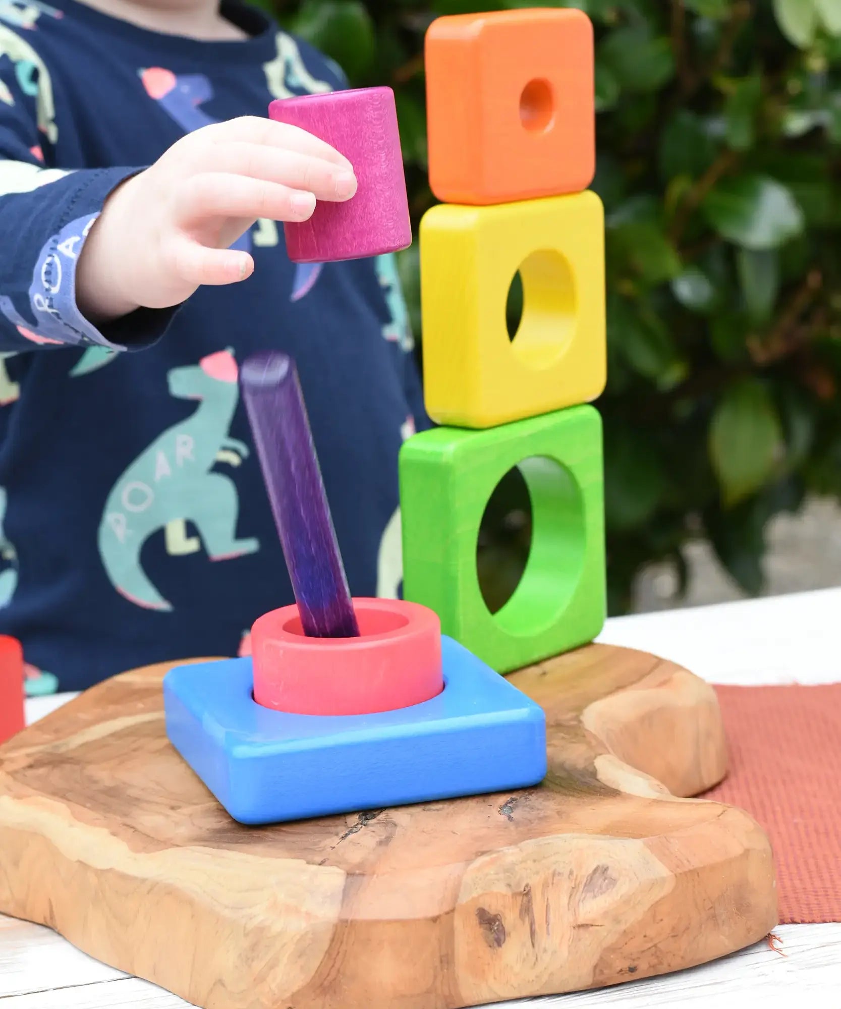 Child playing with the Bajo Puzzle Stacker Tower, lifting the pink cylinder piece that keeps the purple centre pole in place from the base.
