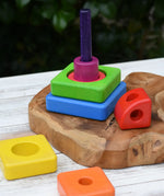 Bajo Puzzle Stacker Tower placed on a  wooden base with some of the pieces placed around the pole and base.