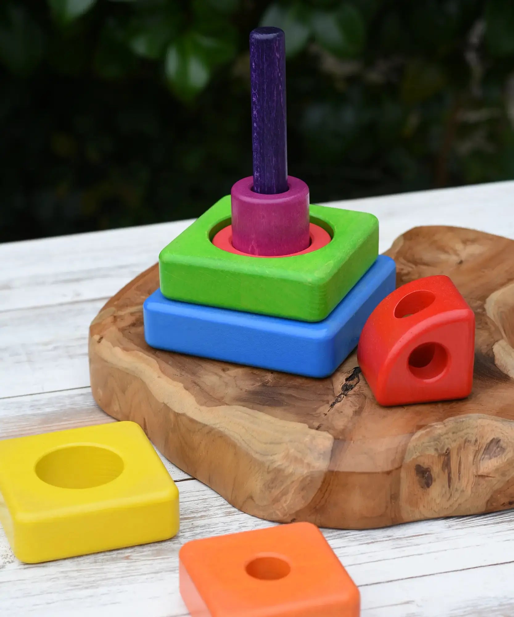 Bajo Puzzle Stacker Tower placed on a  wooden base with some of the pieces placed around the pole and base.
