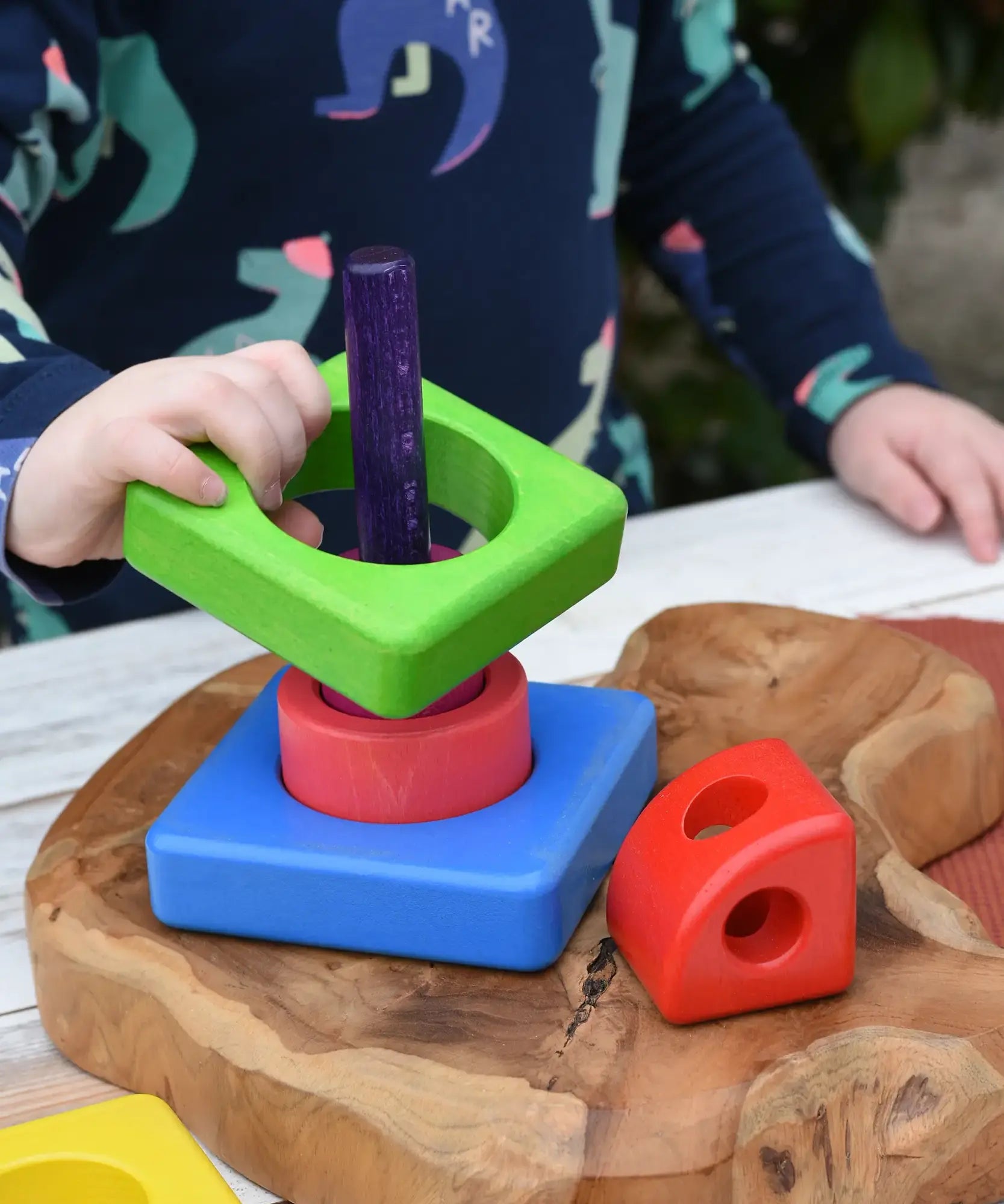 Child placing the pieces from the Bajo Puzzle Stacker Tower on the purple pole.